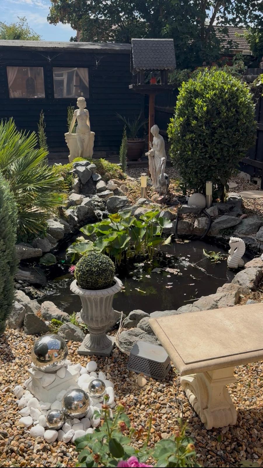 Same garden pond after ELawnCare clearance showing clear water with just a few plants, surrounded by rockery statues and gravel in Cambridge