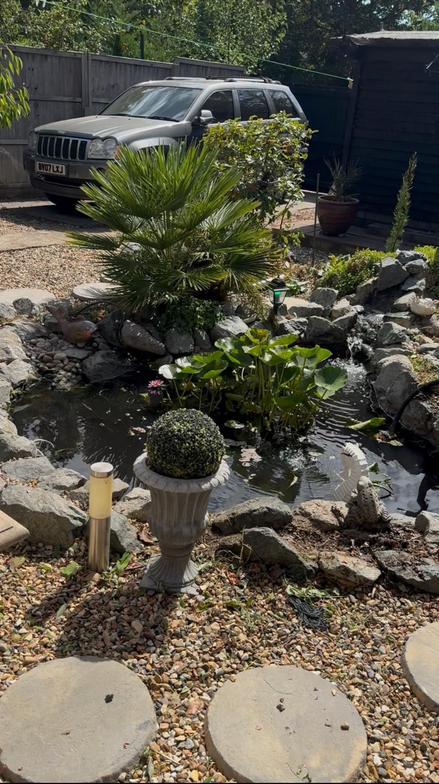 Gravel garden path with stepping stones, chiminea and climbing plants along timber fence in Cambridge